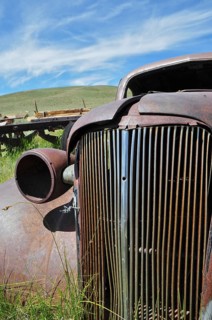 Close-up of a rusty car wreck, Chevrolet Coupé, against blue sky and green area, Bodie Ghost Town,