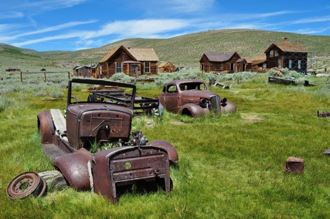 Rusty vehicles, car wrecks, on green area with old abandoned houses, Bodie Ghost Town, California,