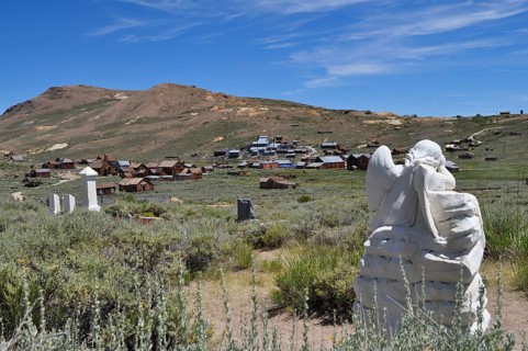 Angel statue in a cemetery overlooking a ghost town in the distance, Bodie Ghost Town, California,