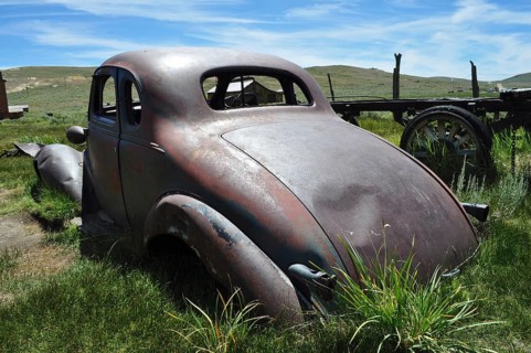 Rear view of an old rusty car wreck, Chevrolet Coupé, on green space in the wilderness, Bodie Ghost