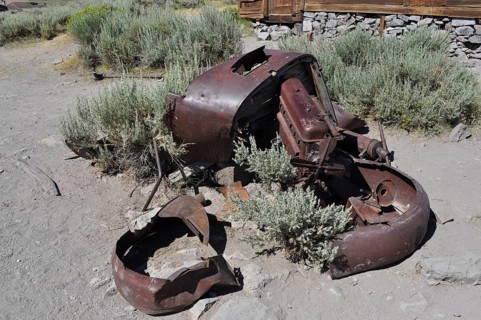 Old crumbling car wreck in a dry landscape with plants, Bodie Ghost Town, California, USA