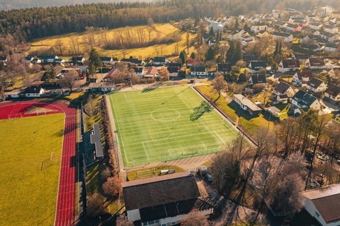 Village with sports field, soccer field and surrounding houses and landscape viewed from the air,