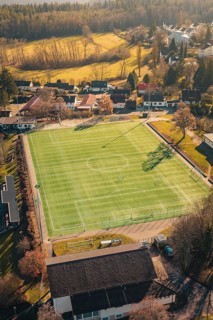 Green soccer field in rural area with surrounding trees and buildings, seen from the air, Wimberg,