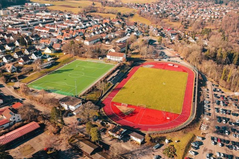 Two sports fields next to each other in a village, shot from the air, with running track and soccer