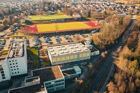 Aerial view of sports ground and school building with adjacent parking lot, nestled in an urban