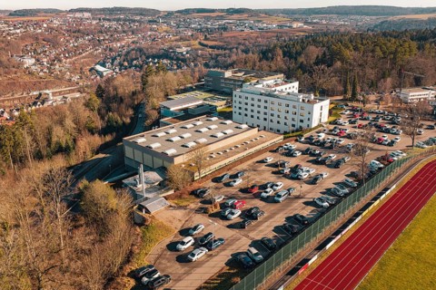 School with parking lot and several cars in a winter landscape with city and hills in the