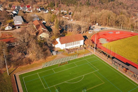 Aerial view of a sports field with red running track and nearby buildings in a village, Wimberg,