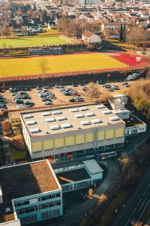 Overview of a sports field with parking lot and school complex in urban and natural surroundings in