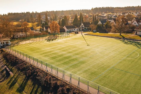 Football field is illuminated by sunlight, surrounded by village houses and trees, Wimberg, Calw,