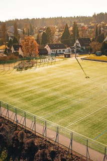 Sunlight illuminates a soccer field in the village with houses and trees in the background,