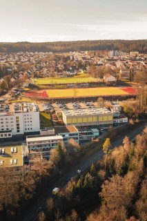 View of a school complex with sports field and playing fields, surrounded by urban landscape and