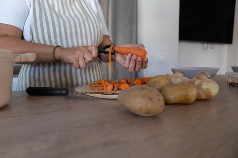 Close up of hands peeling fresh carrot in home kitchen. Healthy ingredients, simple food