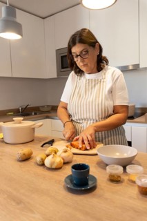 Middle aged woman cooking at home, cutting vegetables on wooden countertop. Simple ingredients,