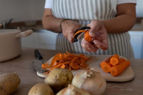 Hands peeling carrots while preparing vegetables at home. Casual lifestyle, healthy ingredients and