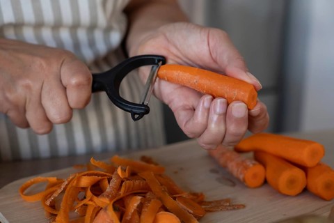 Close up of hands peeling fresh carrot on cutting board in modern kitchen. Simple ingredients,