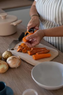 Vertical image of hands peeling carrot in modern kitchen. Casual home cooking, fresh ingredients