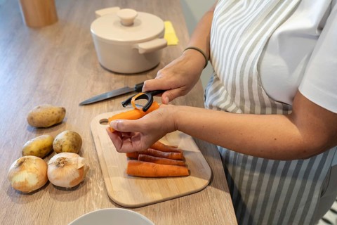 Woman peeling carrots for soup preparation in kitchen. Comfort food, homemade cooking and healthy