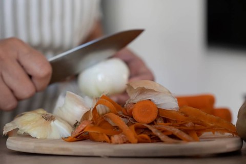 Hands peeling onion while preparing vegetables in kitchen. Casual home cooking, fresh ingredients