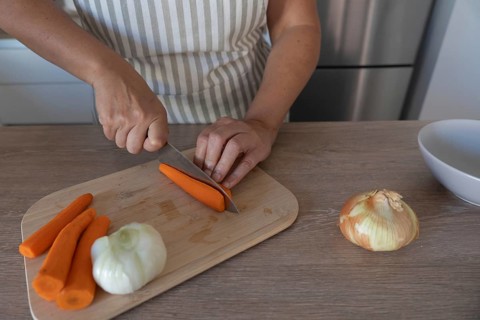 Carrot being cut with a knife on a wooden cutting board while preparing vegetables in a home