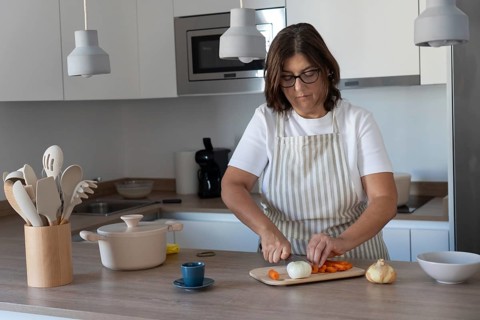 Cozy home kitchen scene with woman wearing apron cutting carrots and preparing vegetables. Comfort