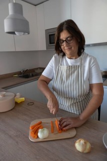 Woman cutting fresh carrots and preparing vegetables for healthy homemade meal in modern kitchen.