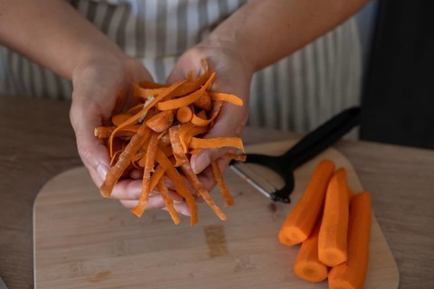 Close-up of hands holding fresh carrot peels while preparing vegetables on a wooden cutting board