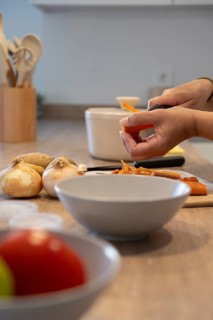 Vertical close up of hands peeling carrot over cutting board. Healthy cooking, fresh vegetables and