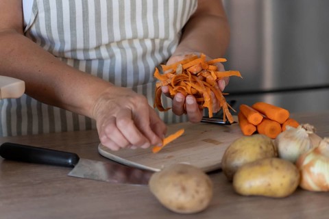 Hands holding freshly peeled carrot skins above a wooden cutting board with whole carrots and
