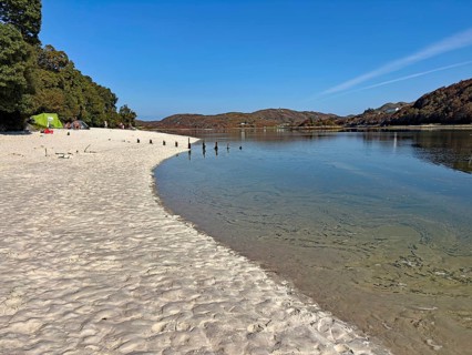 Quiet sandy beach with water views and wooded hills, Silver Sands of Morar, Mallaig, Scotland,