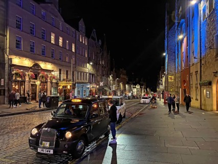 A busy nighttime street scene with a taxi and pedestrians, Royal Mile, Edinburgh, Scotland, United