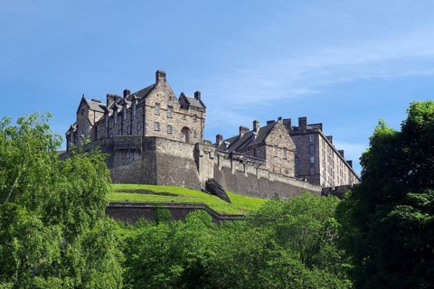 Large historic castle surrounded by greenery, under a blue sky, Edinburgh, Scotland, United Kingdom