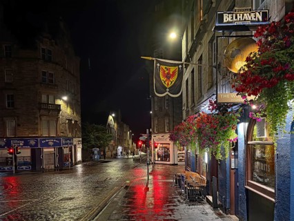 Night view of a quiet city street with wet pavement and illuminated shops. Royal Mile, Edinburgh,