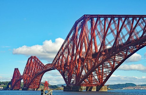 Large red metal bridge against a blue sky with white clouds, railway bridge across the Firth of