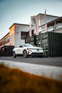 White car in front of an industrial building with containers and flags