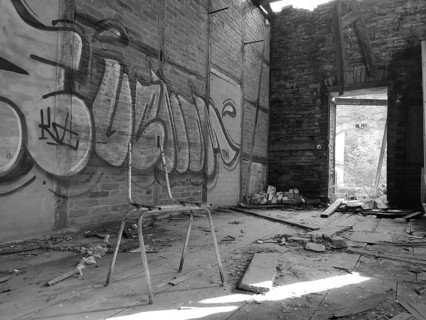 Abandoned room with graffiti and broken ceiling, empty chair ruin in the foreground, monochrome,