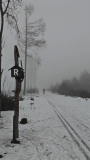 Snowy trail in fog with ski tracks and a lonely cross-country skier in front of the Rennsteig