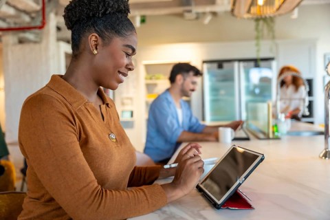 Young professional woman smiling while using a digital tablet and stylus, collaborating with