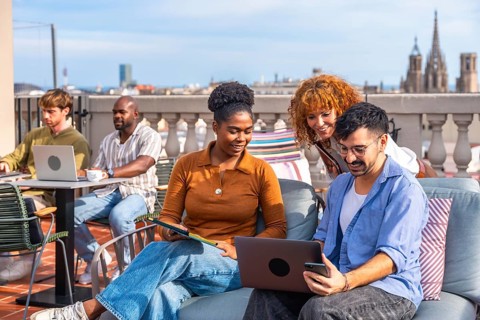 Diverse young professionals collaborating on a modern rooftop terrace, using laptops and