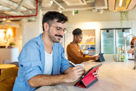 Diverse individuals making notes on a digital tablet and drinking coffee in a modern coworking