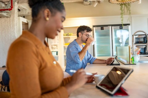 Coworkers are enjoying a coffee break in a modern co working space, using tablets for work or