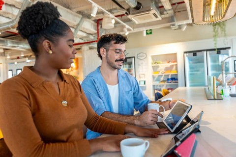 Diverse colleagues in a modern office breakroom are collaborating and discussing work using digital