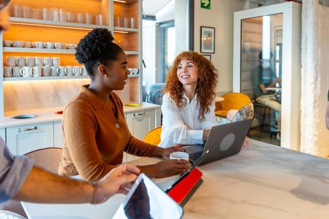 Multiracial businesswomen colleagues collaborating and discussing work around a laptop in a modern