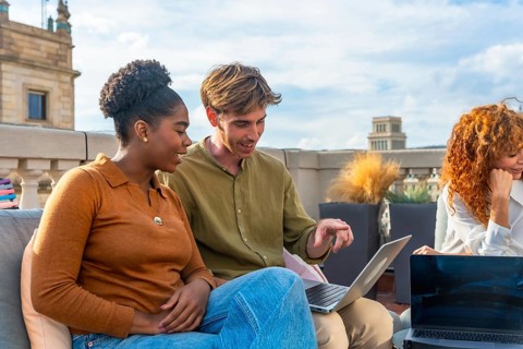 Diverse colleagues collaborate on a laptop during a rooftop meeting, sharing ideas and planning in