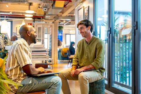 Two diverse male colleagues collaborate and chat during an informal break in a modern coworking