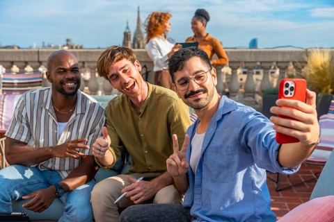 Diverse team of colleagues smiling and taking a rooftop selfie on a sunny urban terrace during a