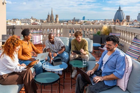 Diverse colleagues brainstorm and collaborate on laptops and tablets on a vibrant rooftop terrace