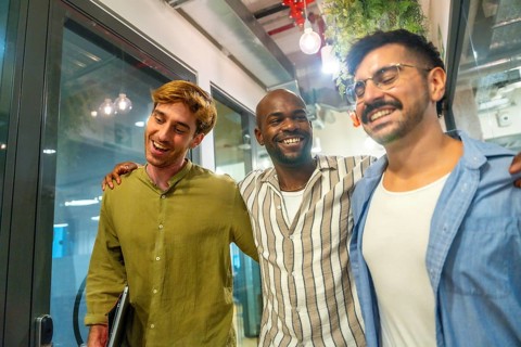Multi ethnic male colleagues walking and laughing in a modern coworking space, sharing a friendly