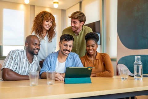 Diverse business team members gathering around a digital tablet, smiling and collaborating while