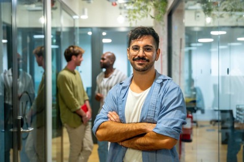 Confident male professional standing with arms crossed, smiling at the camera while his multi