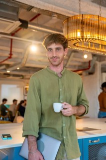 Young man standing in a modern coworking office, enjoying a coffee break while holding a laptop,